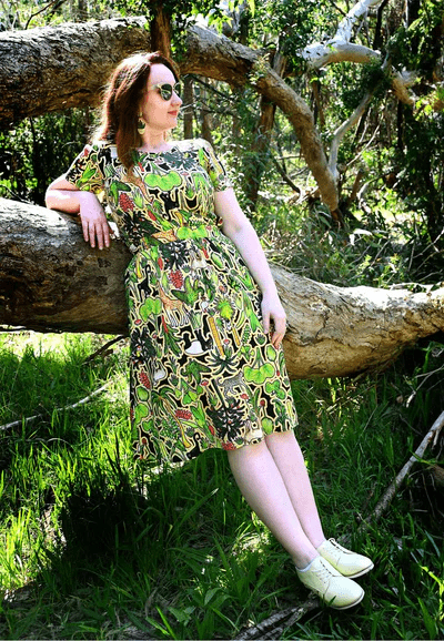 This dress showcases a complex pattern with elements of flora, including leaves, flowers, and abstract natural shapes in shades of green, red, and yellow. The design appears dense and rich, resembling an intricate forest scene. Designed by Australian designer brand Streborclothing.