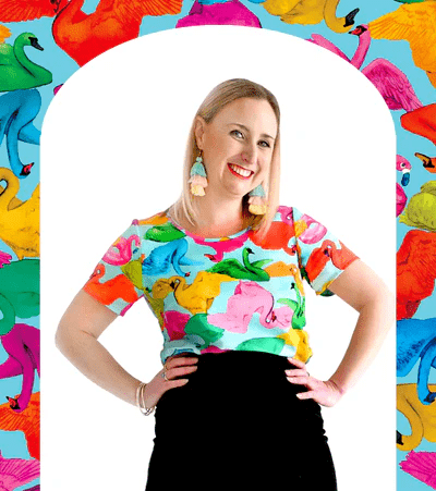 A colorful top displaying an abstract pattern of vibrant swans in reds, greens, and pinks, against a light blue background, with each swan in a unique position, adding movement and whimsy. Designed by Australian designer brand Streborclothing.
